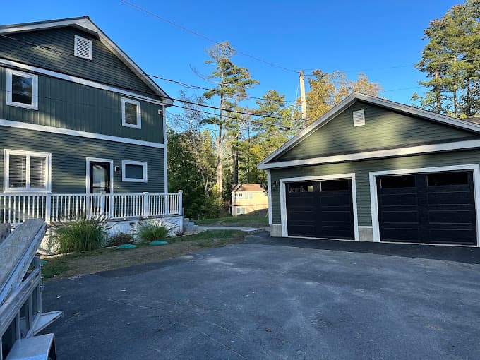Two car garage with black doors, built onto a green clapboard house